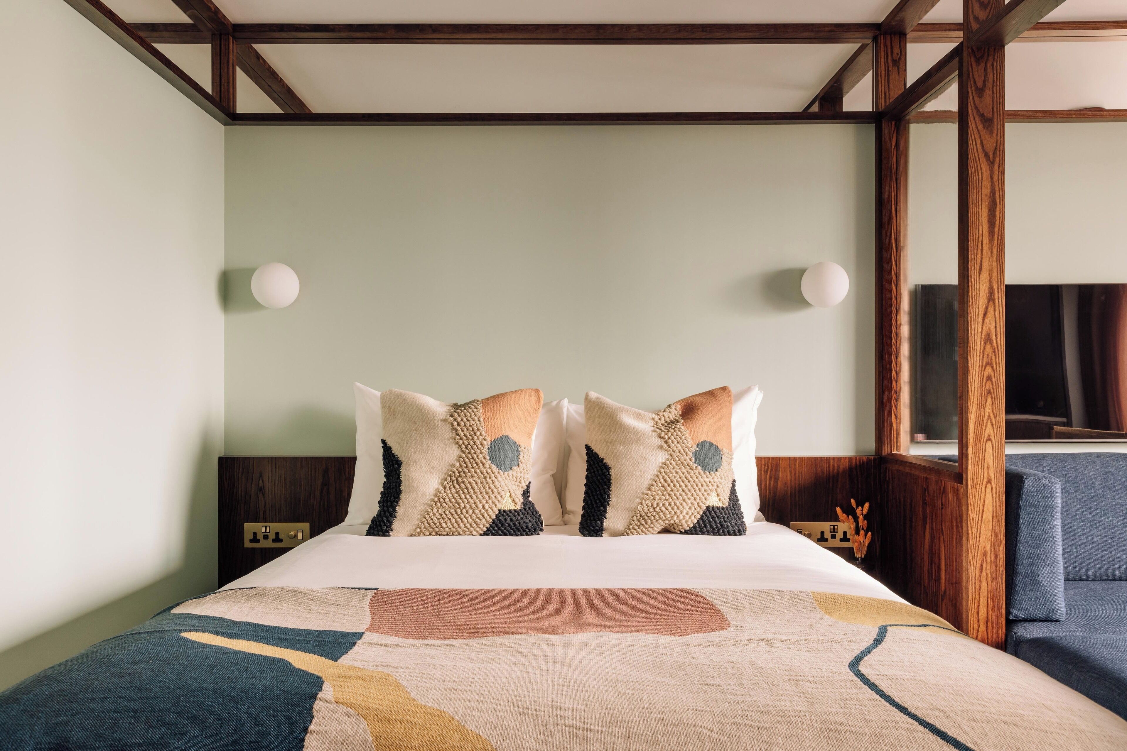 Un lit bien fait, recouvert d’une couvre-lit à motifs géométriques, agrémenté de deux coussins décoratifs et d’une table de chevet dotée d’une prise électrique.