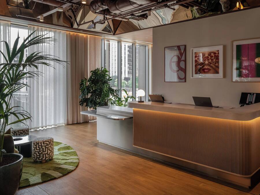 A reception desk with a modern design, large windows with curtains, and a view of the cityscape.