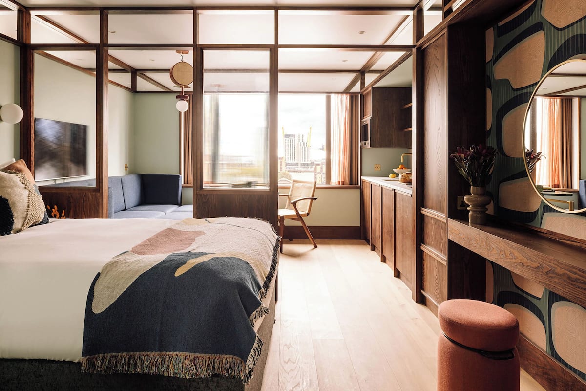 Ein modernes Schlafzimmer mit großem Bett, einer Sitzecke, einem Schreibtisch und Blick auf die Stadt.