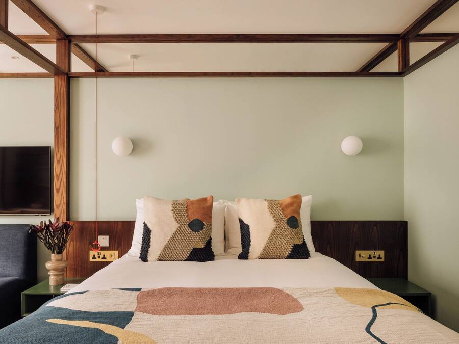 A hotel room with a bed, a nightstand, a wall-mounted TV, and a power outlet.