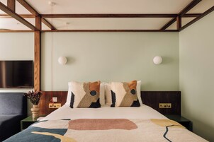 Habitación de hotel con cama, mesita de noche, televisor montado en la pared y toma de corriente.