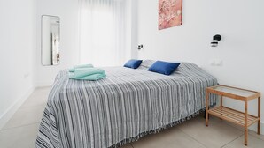 Een slaapkamer met een bed, nachtkastje, spiegel, raam met gordijnen en een wandlamp.