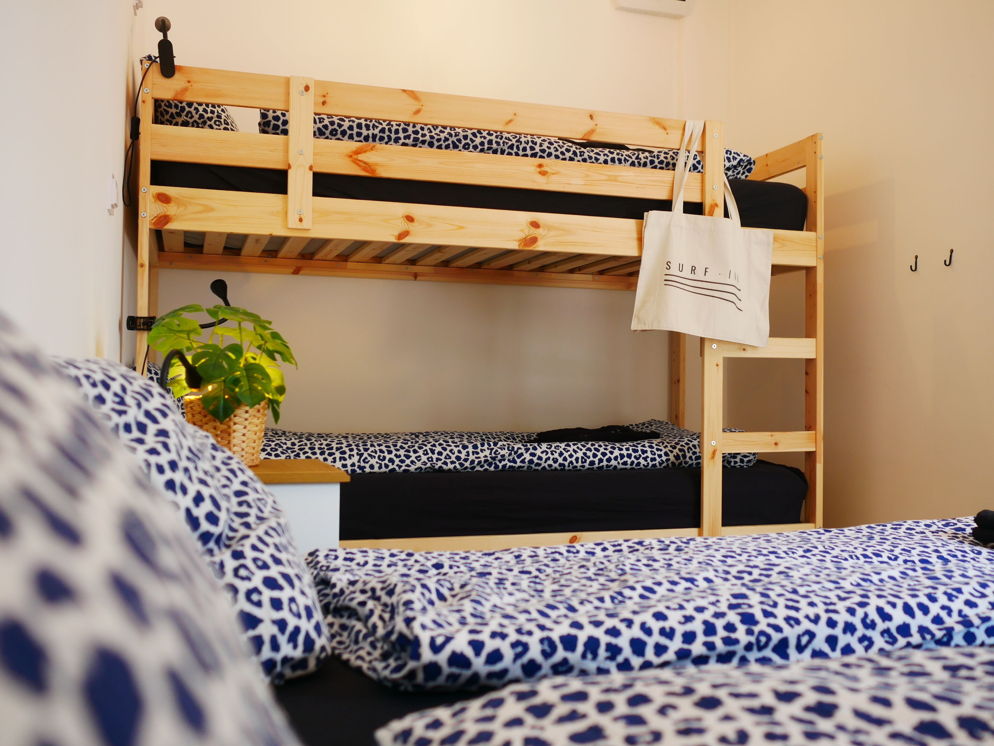 A bunk bed room with a leopard print bedspread, a small bedside table with a plant, and a white tote bag hanging on the bunk bed.
