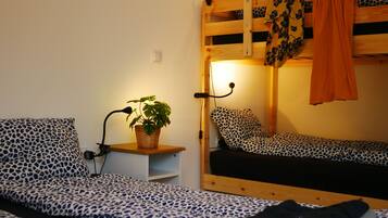 Un dormitorio con literas, una mesita de noche con lámpara y una planta en maceta.