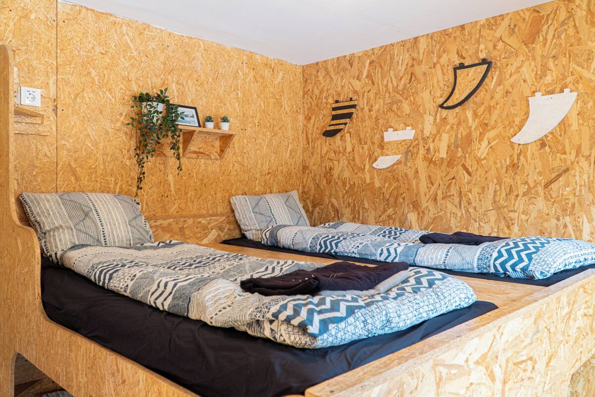 Ein Zimmer mit zwei Betten, Holzwänden, einem Regal mit Pflanzen und Wandbildern.