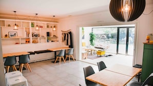 A modern dining area with a long bench, wooden tables, and black chairs. There are hanging lights and a view of the outdoors through a glass door. - SURFinn Vieux Boucau (Vieux-Boucau-les-Bains)