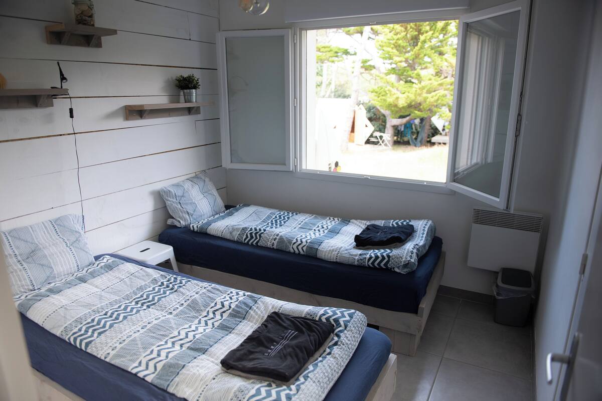 Ein Schlafsaalzimmer mit zwei Betten, einem Fenster und einem kleinen Regal mit einer Pflanze.