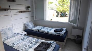 A dorm-style room with two beds, a window, and a small shelf with a plant.
