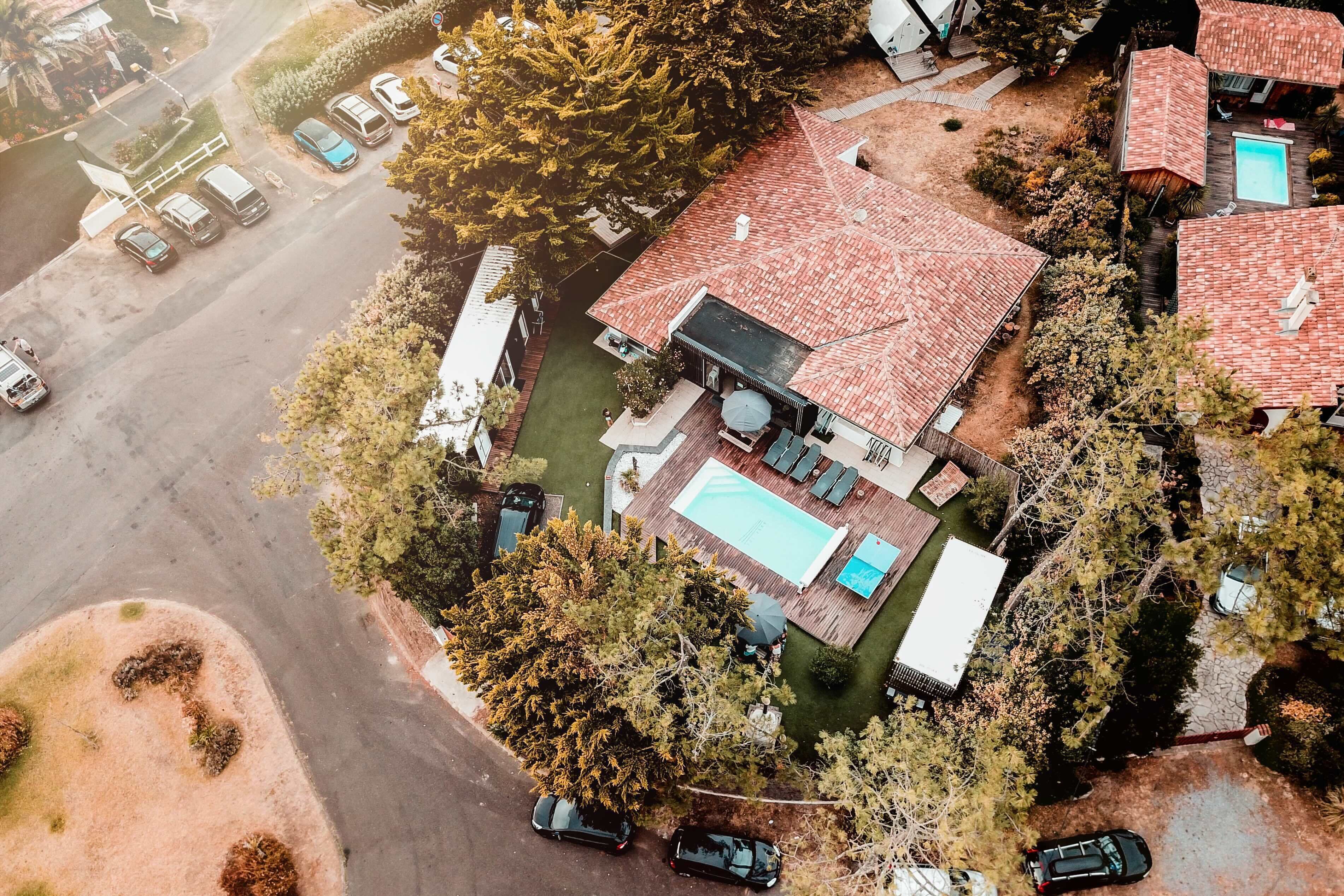 An aerial view of a residential property with a swimming pool, multiple cars, and a large tree.