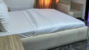 Ein Hotelzimmer mit einem Bett, einem Schreibtisch und einem Sessel. An der Wand ist eine Klimaanlage angebracht.