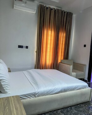 A hotel room with a bed, a desk, and a chair. There is an air conditioning unit on the wall. - Lakehouse Apartment (Abuja)