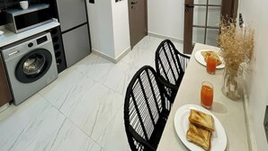 Eine kleine Küche mit modernen Geräten, ein Essbereich mit Tisch und Stühlen sowie ein Flur, der zu einer Tür führt.