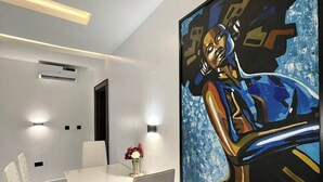 Ein zeitgemäßer Essbereich mit einem weißen Tisch, Stühlen und einem großen abstrakten Gemälde an der Wand.