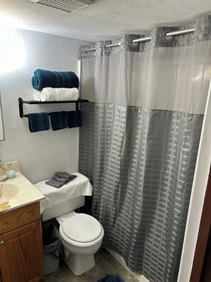 A bathroom with a toilet, a sink, a towel rack with towels, and a shower curtain. - Adventures Start Here-Walk to Slopes (Angel Fire)