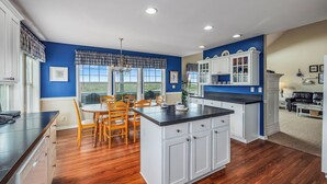 A kitchen with a central island, wooden chairs, and a dining table. - NEW! Ocean View, Hot Tub, Game Room (Nant@Beach) (Ocean Park)