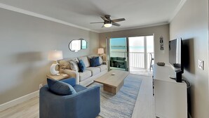 Un soggiorno moderno con divano, tavolino da caffè e TV, che si apre su un balcone con vista sulla spiaggia.