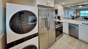 Una cucina moderna con lavatrice e asciugatrice integrate, elettrodomestici in acciaio inossidabile e vista sull'area soggiorno.