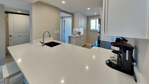 Una cucina moderna con mobili bianchi, un'isola ampia con lavello e una macchina per il caffè.