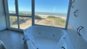 Een badkamer met een groot bad, uitzicht op het strand en een raam.