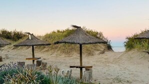 Een strand met rieten parasols en houten banken.