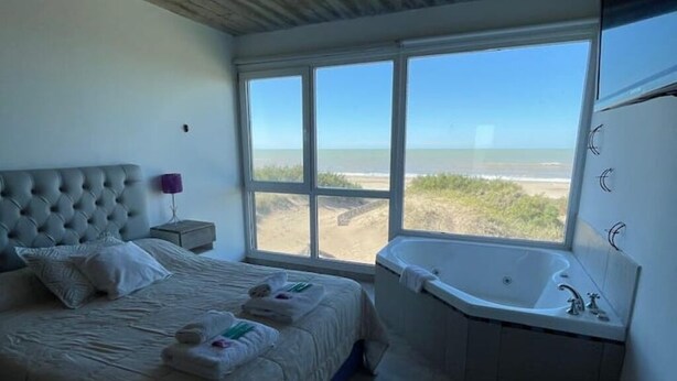 Een slaapkamer met een groot bed, een badkuip en uitzicht op het strand.