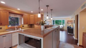 A modern kitchen with granite countertops, wooden cabinets, a built-in oven, and pendant lighting.