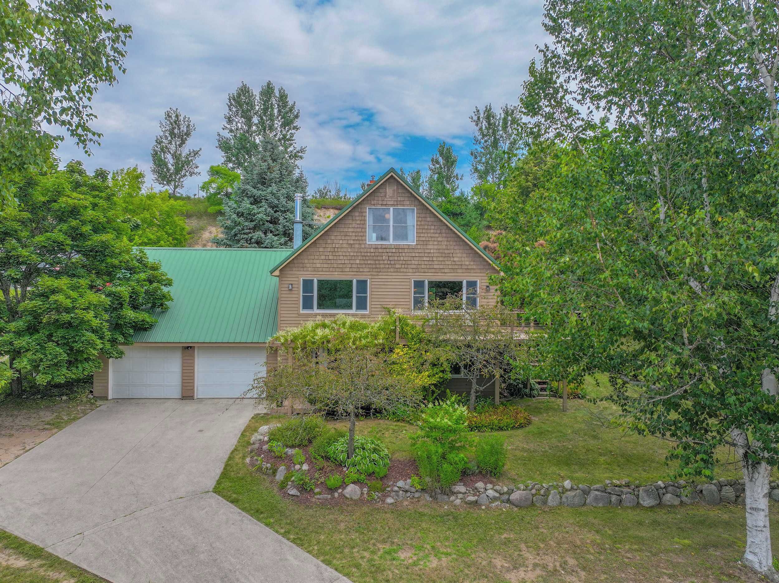 A two-story house with a green roof, a garage, and a well-maintained garden with various plants and a stone border.