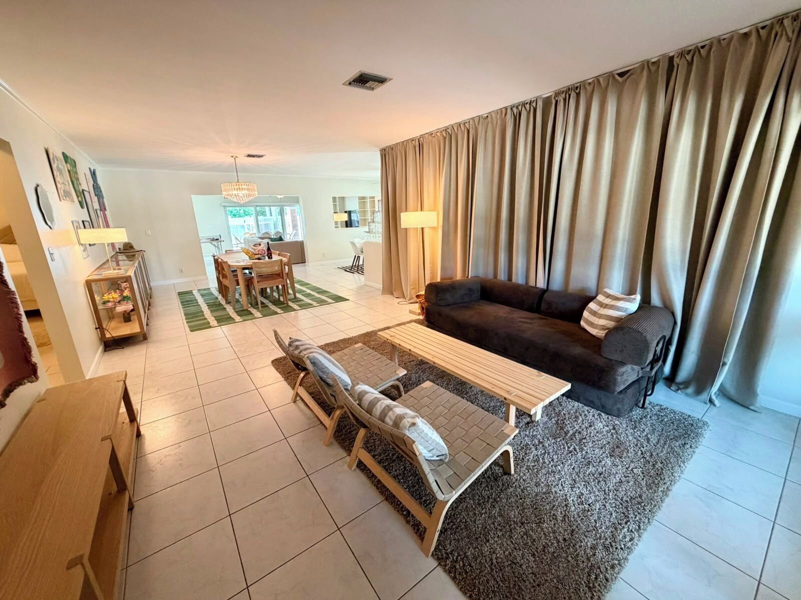 A living room with a sofa, a coffee table, a dining area with chairs, and a kitchen in the background.
