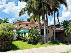 A two-story house with a tiled roof, surrounded by lush greenery and palm trees. - Luxury Hollywood Lakes Villa (Hollywood)