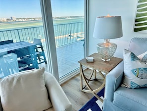 A balcony with a view of the sea and buildings, a table with chairs, a lamp, and a sofa with cushions. - Luxury Bayfront Retreat at Caribe Resort (Orange Beach)
