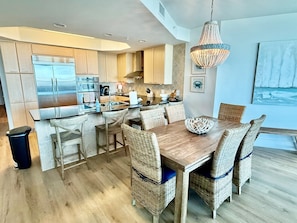 A modern kitchen with stainless steel appliances, a dining area with wicker chairs, and a large chandelier. - Luxury Bayfront Retreat at Caribe Resort (Orange Beach)