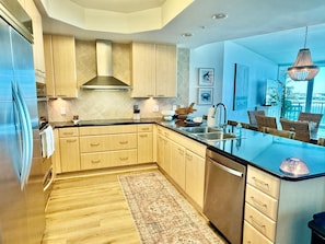 A modern kitchen with wooden cabinets, a stainless steel refrigerator, and a large island with a sink. - Luxury Bayfront Retreat at Caribe Resort (Orange Beach)
