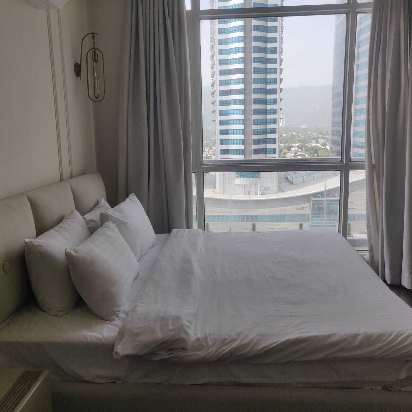 Een hotelkamer met een groot bed, uitzicht op een hoog gebouw en een raam met gordijnen.