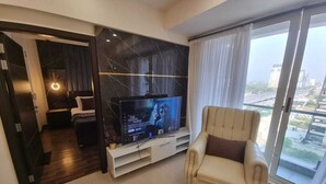Un salon moderne doté d’un téléviseur à écran plat, d’un fauteuil en cuir et d’une grande fenêtre donnant sur la ville.