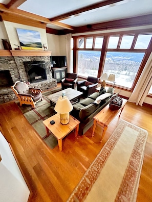 A cozy living room with a stone fireplace, comfortable seating, and a large window offering a scenic view.