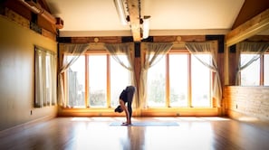 A spacious room with large windows, wooden beams, and a yoga mat on the floor.