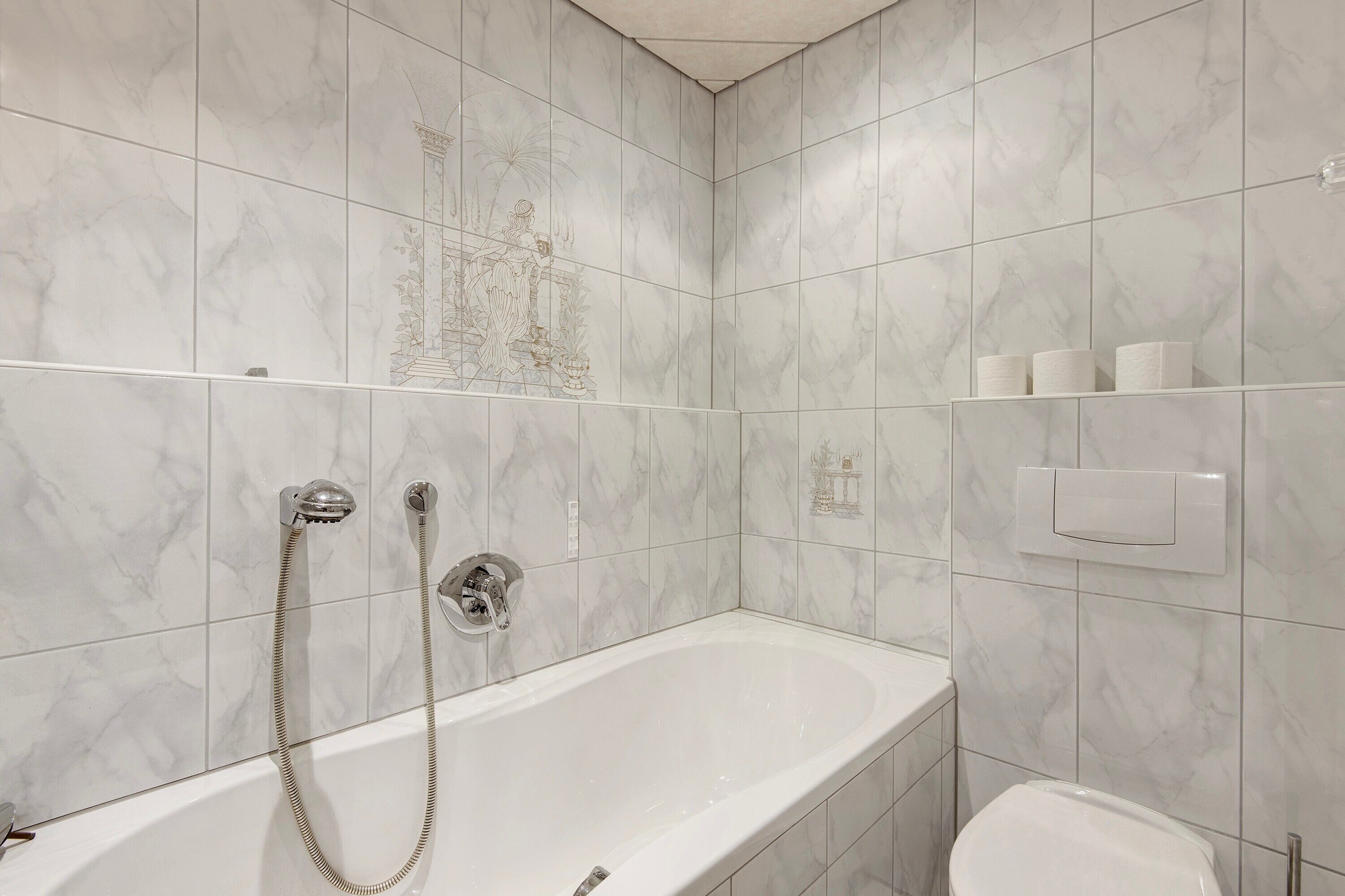 A bathroom with a bathtub, shower, toilet, and marble tiles.