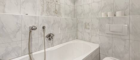 A bathroom with a bathtub, shower, toilet, and marble tiles.