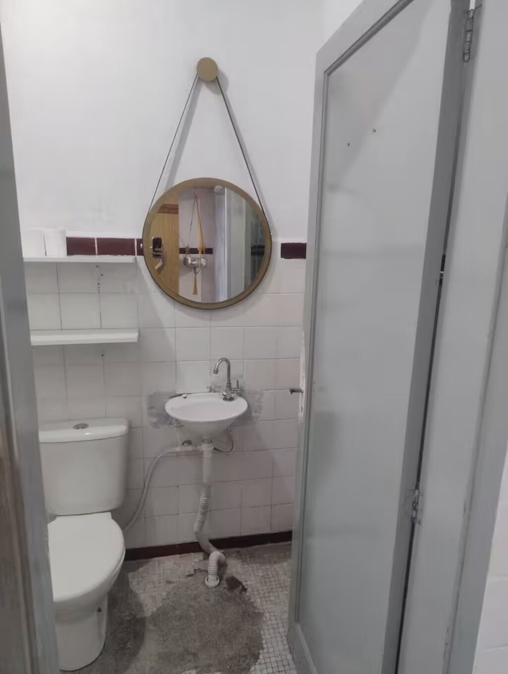 Une petite salle de bain comprenant des toilettes, un lavabo et un miroir fixé au mur.