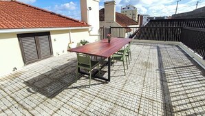 Una terrazza sul tetto con un tavolo e sedie di legno, una pianta in vaso e vista su edifici con tetti in tegole rosse.