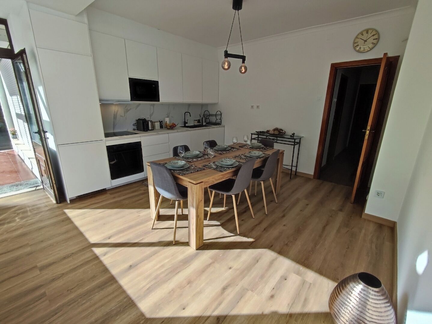 A modern kitchen with white cabinets, a dining table set for six, and a clock on the wall.