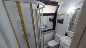 A bathroom with a glass shower enclosure, a toilet, a sink, and a mirror with lights.
