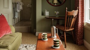 A cozy living room with a wooden coffee table, a green sofa, a wooden chair, and a view of a bathroom with a towel rack and a mirror. - The Great Decoy (Hurstbourne Tarrant)