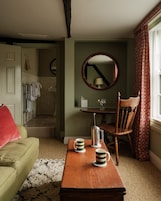 Un salón acogedor con una mesa de centro de madera, un sofá verde, una silla de madera y vistas a un baño con toallero y espejo.