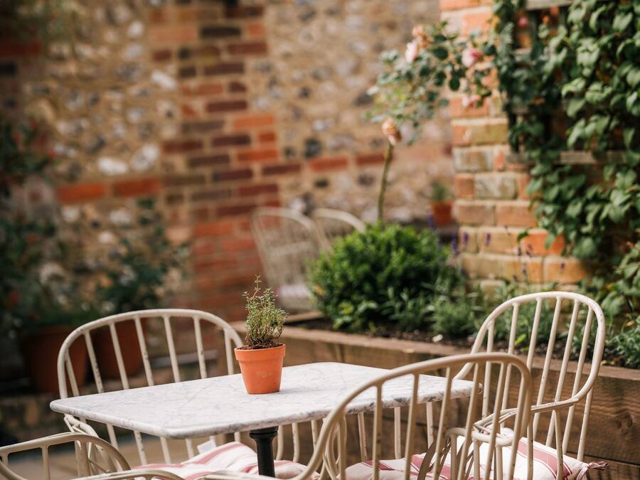 Un patio con mesa y sillas, una planta en maceta y un muro de ladrillo con plantas.