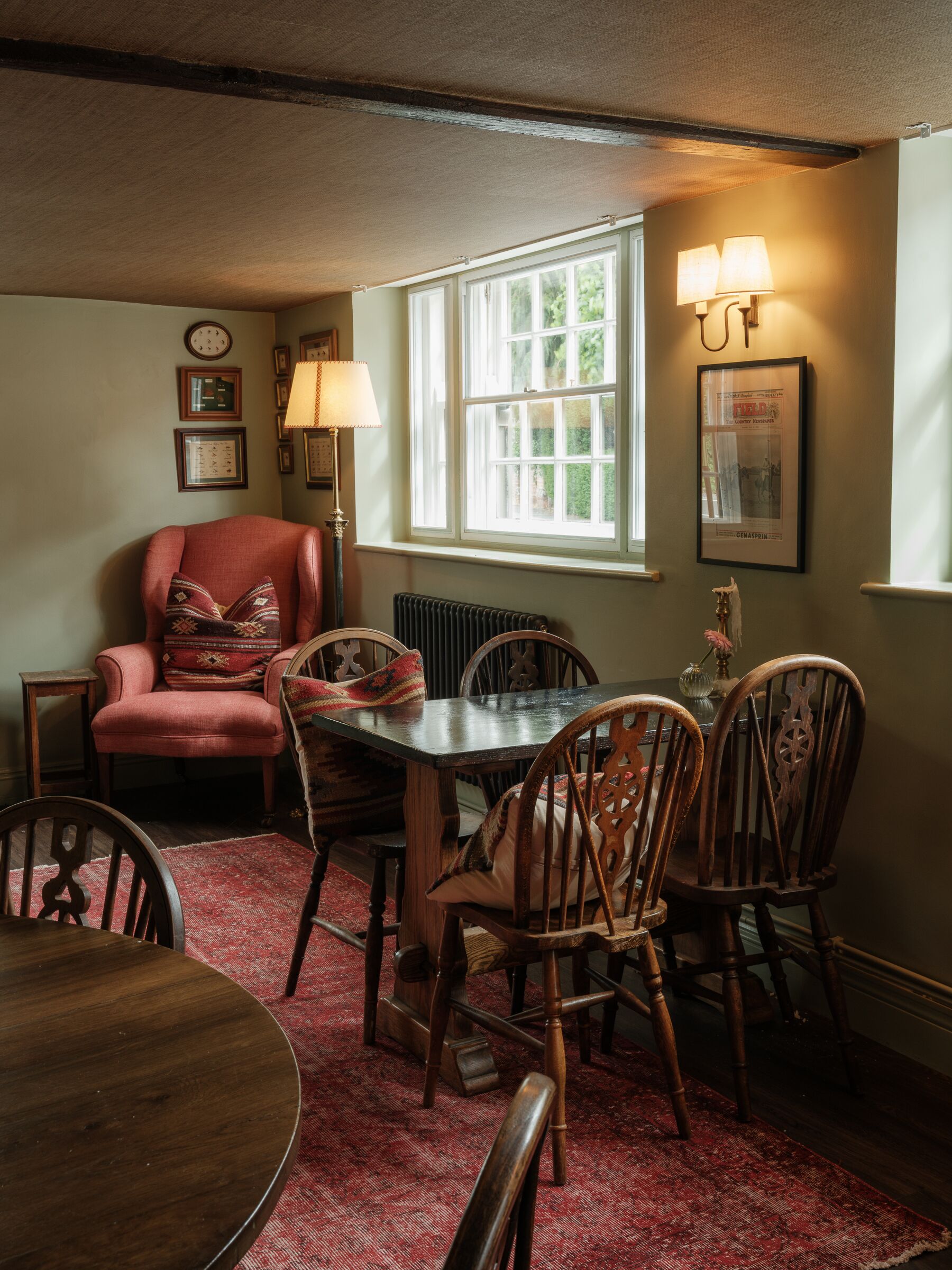 A dining area with a table, chairs, a red armchair, a radiator, and a window with natural light.