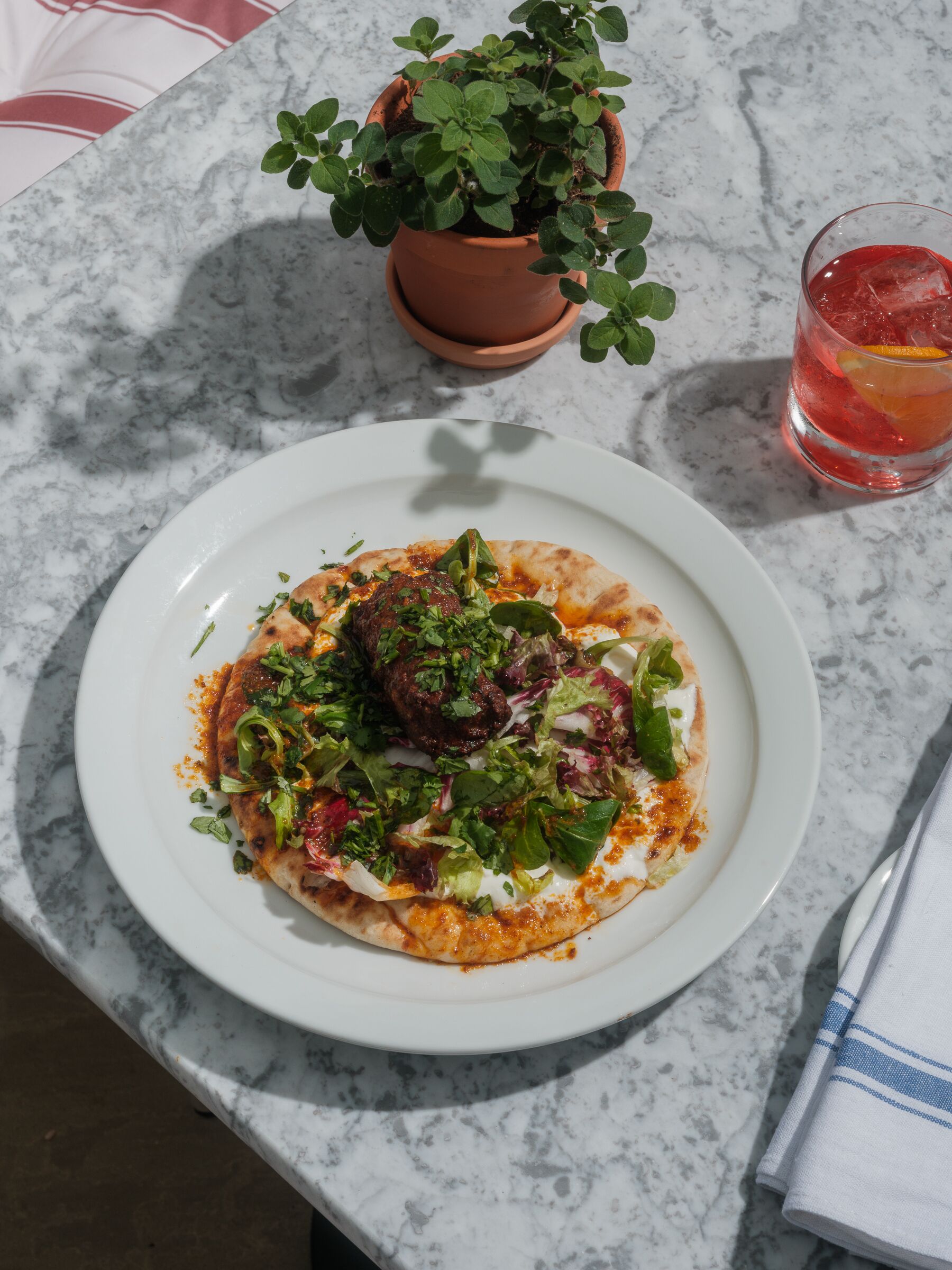 Un plato de comida, un vaso de bebida y una planta en maceta sobre una superficie de mármol.