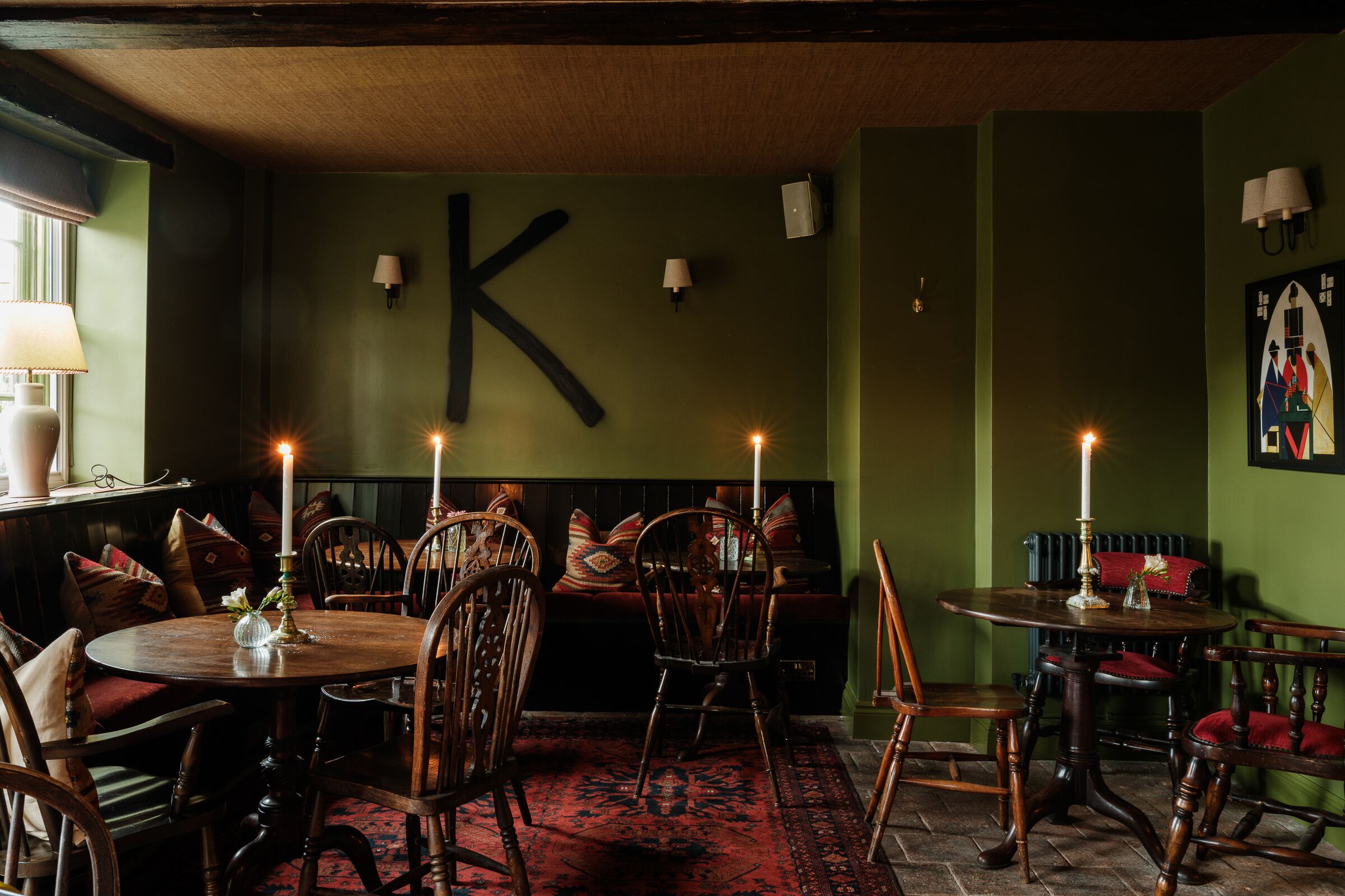 Une pièce avec un grand « K » peint sur le mur, des meubles en bois et un tapis rouge à motifs.