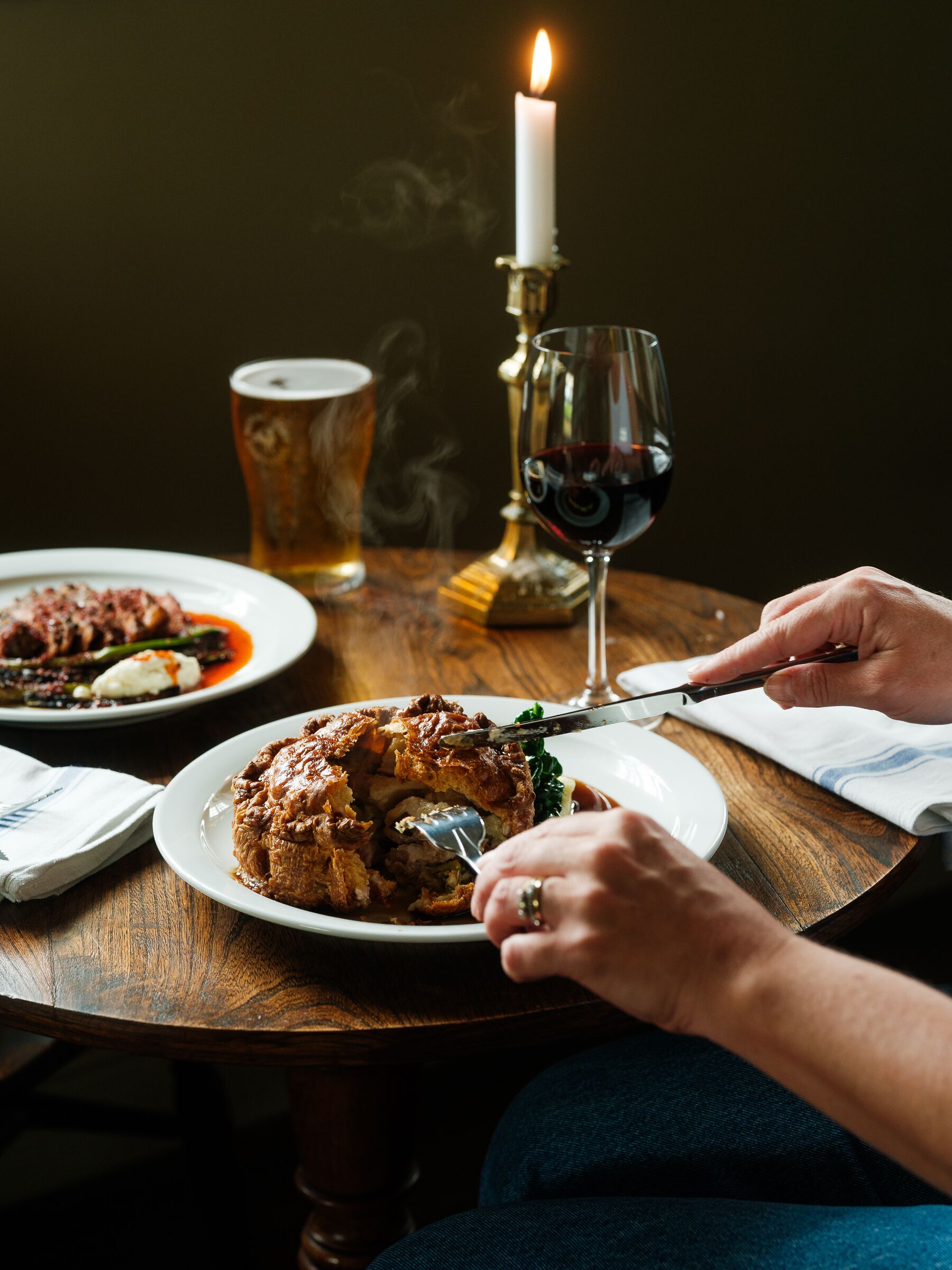 A dining table with a plate of food, a glass of red wine, and a candle.
