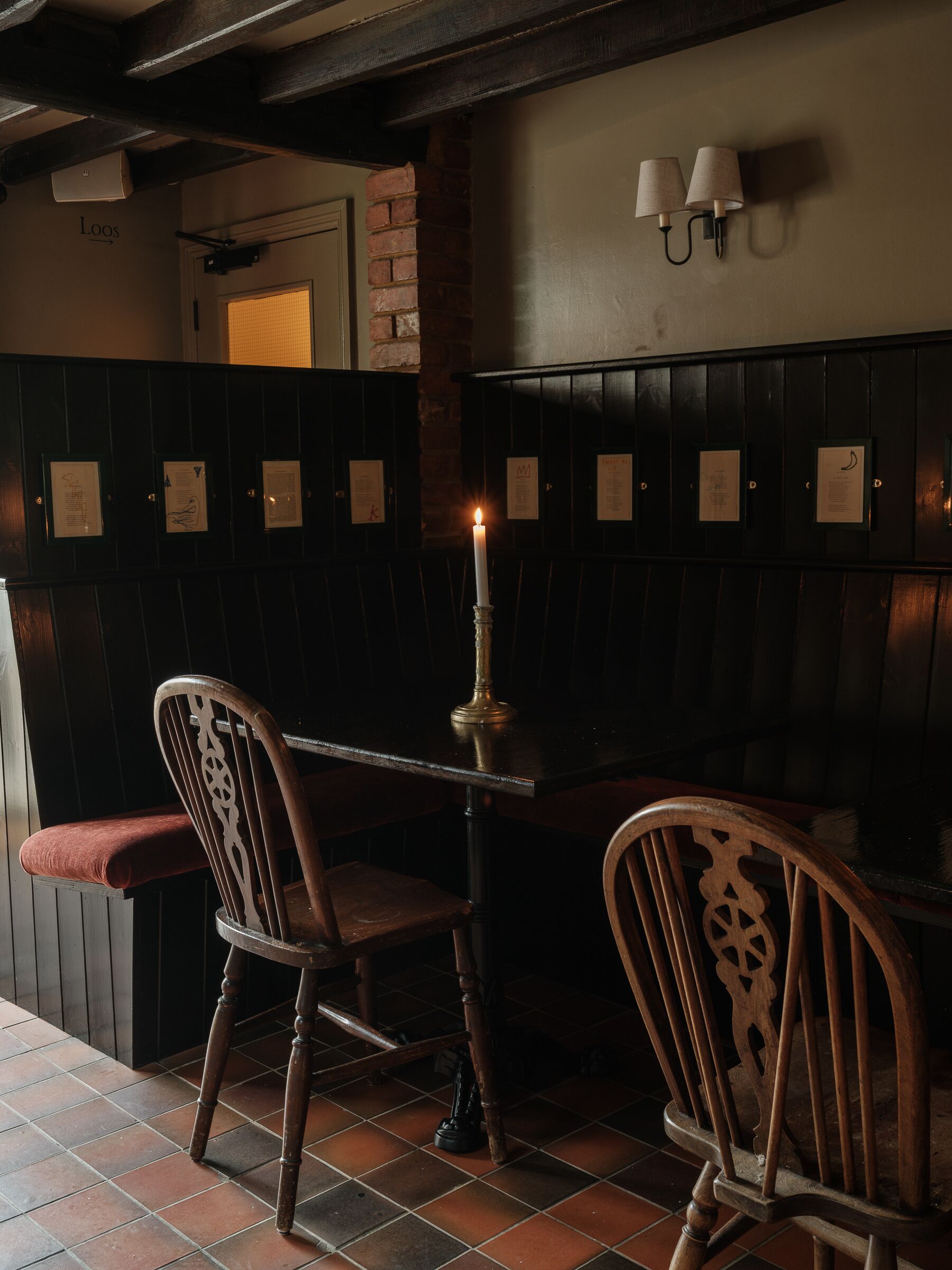 Un ristorante scarsamente illuminato con sedute in legno, un tavolo con una candela e menu esposti alle pareti.